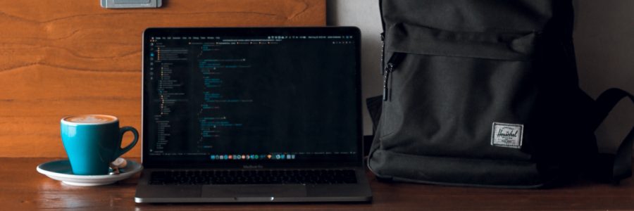 computador com código aparecendo ao lado de uma xícara e uma mochila