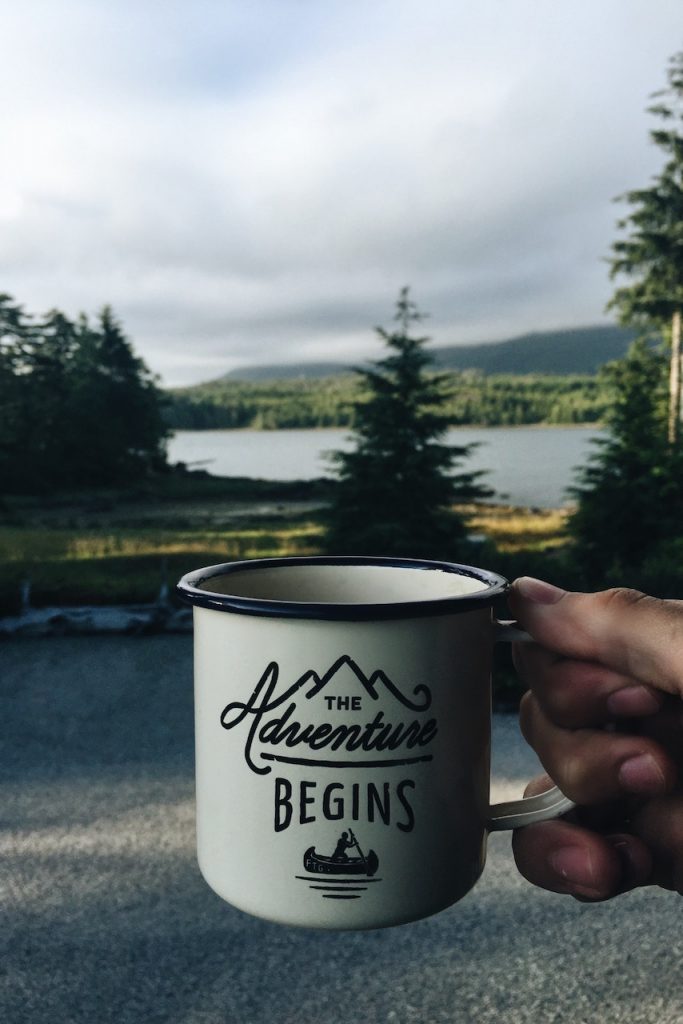 Pessoa segurando caneca escrito "The adventure begins"