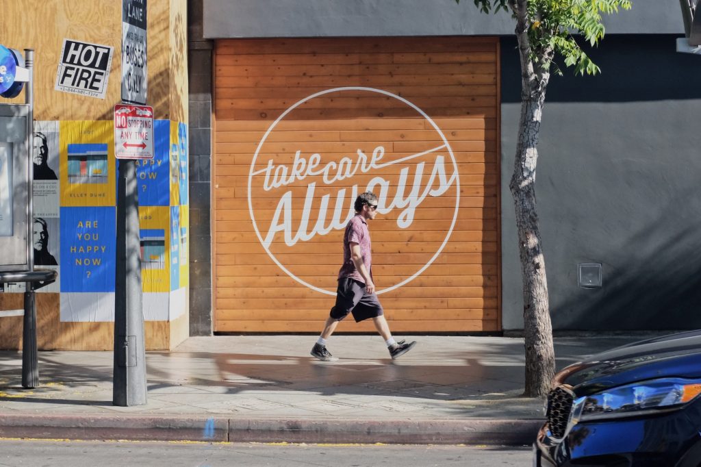 homem caminhando, loja com dizeres 'take care always' ao fundo